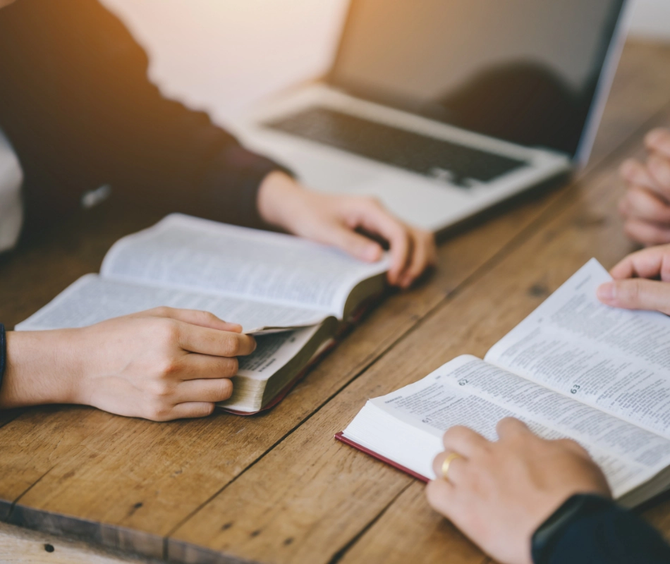 Three people studying at a wooden table, with two open Bibles and a laptop visible; it's a perfect setting to connect with a Christian church for deeper understanding and community.